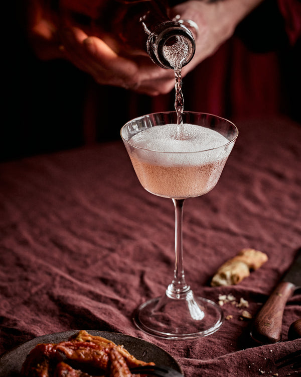 Cocktail being poured into a glass with a dark background